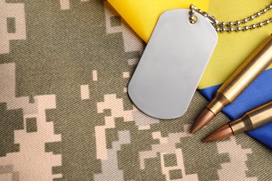 Military ID tag, bullets and Ukrainian flag on pixel camouflage, flat lay. Space for text