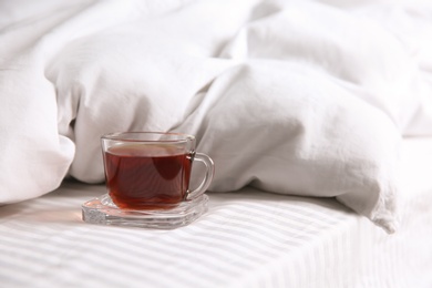 Glass cup with black tea near soft blanket on bed