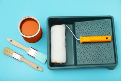 Photo of Can of orange paint, brushes, roller and container on turquoise background, flat lay