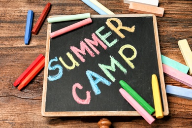 Little blackboard with text SUMMER CAMP chalked in different colors on table