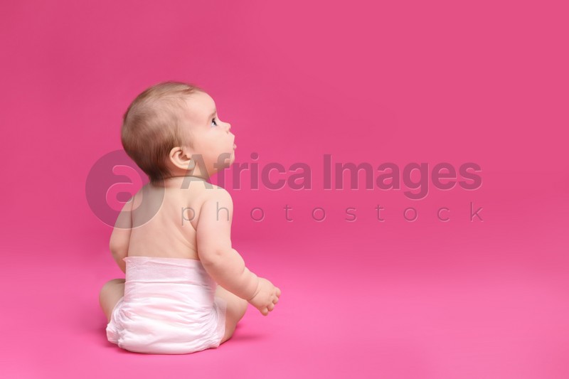 Cute little baby in diaper sitting on pink background, back view. Space for text