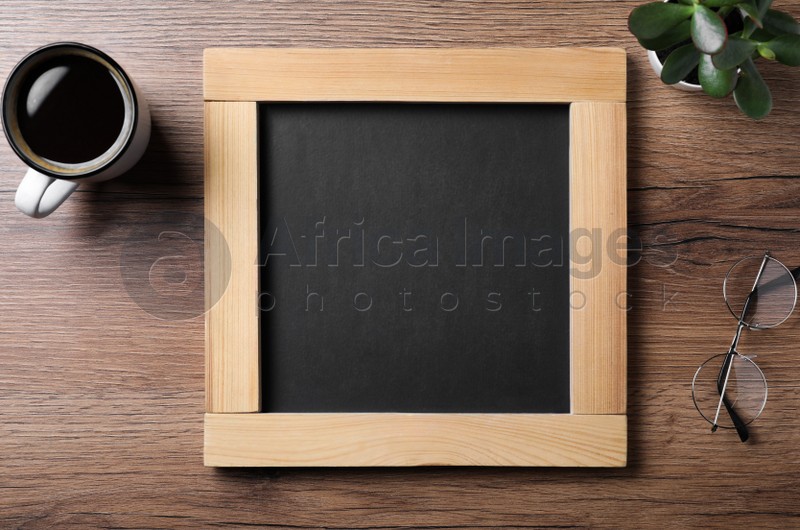 Clean small blackboard, coffee, chalk and glasses on wooden table, flat lay