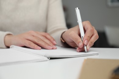 Left-handed woman writing in notebook at table indoors, closeup