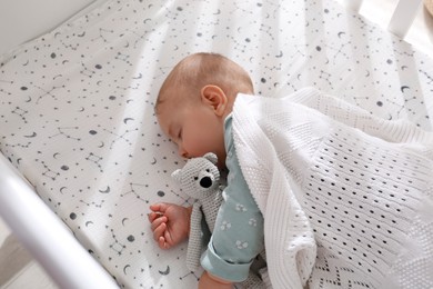 Photo of Adorable baby with toy peacefully sleeping in crib, above view