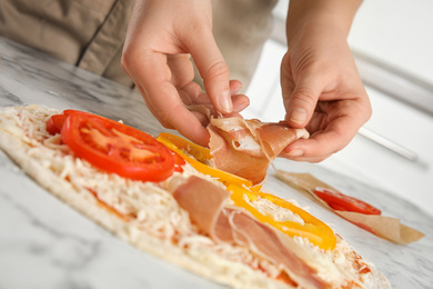Woman adding prosciutto to pizza white marble table, closeup