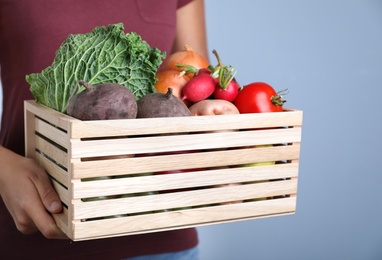 Farmer with wooden crate full of different vegetables and fruits on blue background, closeup. Harvesting time