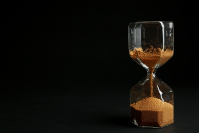 Hourglass with golden sand on black background. Space for text