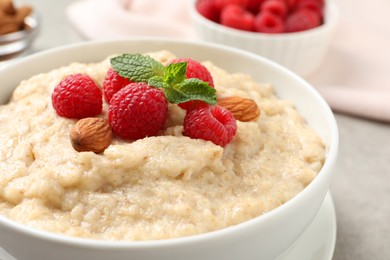 Tasty oatmeal porridge with raspberries and almond nuts in bowl on table, closeup