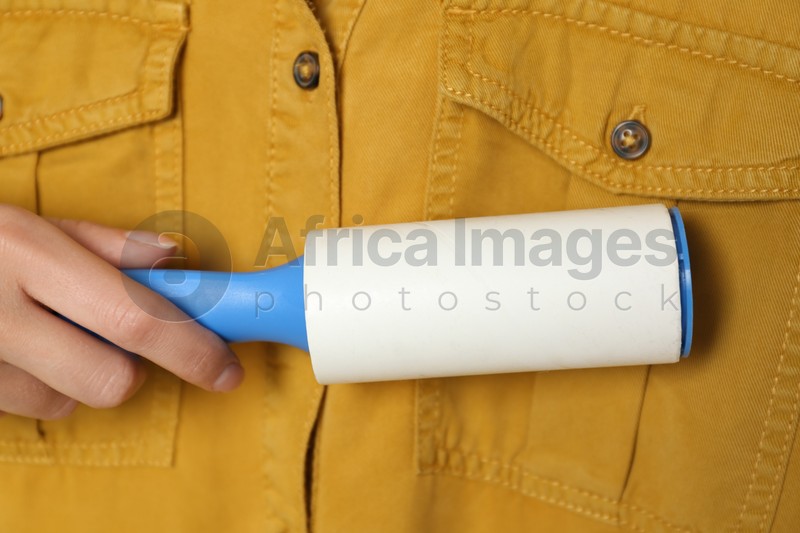Photo of Woman cleaning yellow shirt with lint roller, closeup