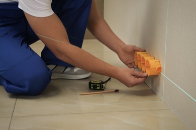 Worker using cross line laser level for installation of outlet box in plasterboard, closeup