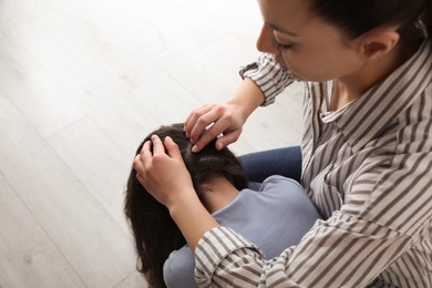 Mother examining her daughter's hair indoors. Anti lice treatment