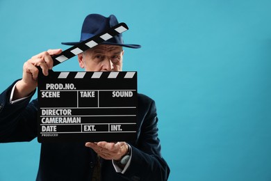 Photo of Senior actor holding clapperboard on light blue background, space for text. Film industry
