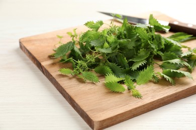 Wooden board with fresh stinging nettle leaves on white table, closeup
