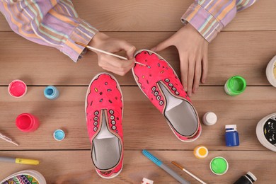 Woman painting on sneaker at wooden table, top view. Customized shoes
