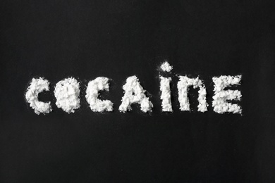 Word Cocaine written with white powder on black background, top view