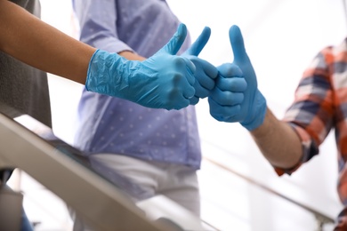Group of people in blue medical gloves showing thumbs up on light background, closeup