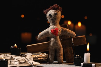 Voodoo doll with pin in heart and ceremonial items on wooden table against blurred background