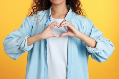 African-American woman making heart with hands on yellow background, closeup