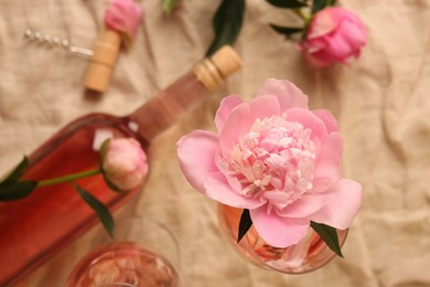Beautiful pink peony in glass of rose wine on beige fabric, top view