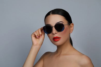 Attractive woman wearing fashionable sunglasses against grey background