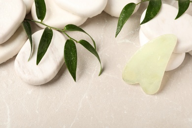Photo of Jade gua sha tool, green branches and spa stones on grey table