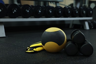 Yellow medicine ball, weighting agents and dumbbells on floor in gym, space for text