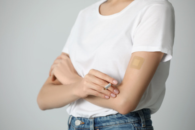 Young woman with nicotine patch and cigarette on light grey background, closeup