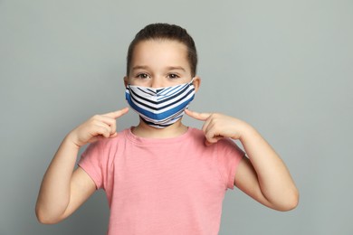 Cute little girl in protective mask on grey background