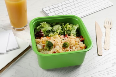 Photo of Container with tasty food, cutlery, keyboard, glass of juice and notebooks on white wooden table. Business lunch