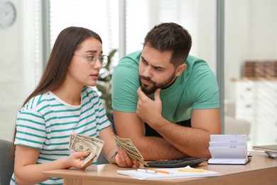 Worried young couple counting money at wooden table indoors