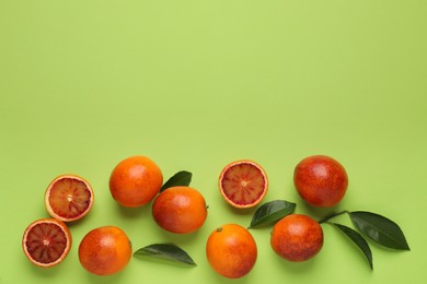 Many ripe sicilian oranges and leaves on light green background, flat lay. Space for text