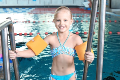 Little girl with swimming sleeves in indoor pool