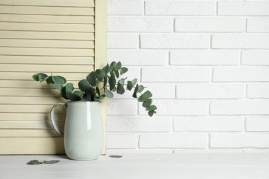 Beautiful eucalyptus branches in vase on white wooden table. Space for text