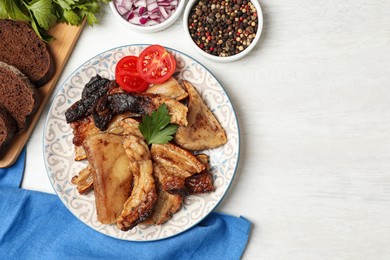 Tasty fried pork lard with parsley and tomatoes on white wooden table, flat lay. Space for text