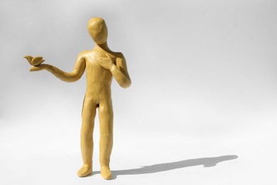 Yellow plasticine human figure with dove on white background, space for text