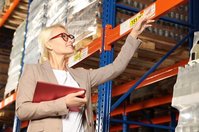 Happy manager using modern tablet and pointing at something in warehouse with lots of products, low angle view