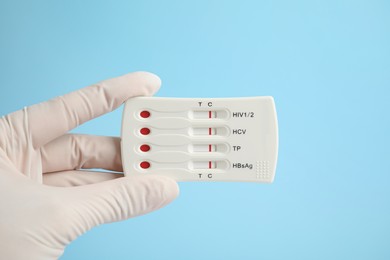 Doctor holding disposable express test for hepatitis on light blue background, closeup