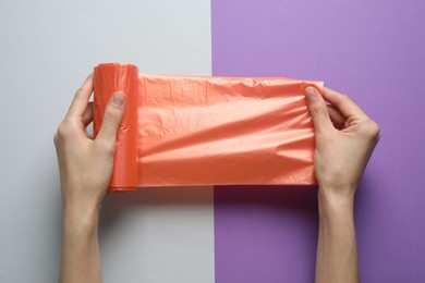 Photo of Woman holding roll of orange garbage bags over color background, top view