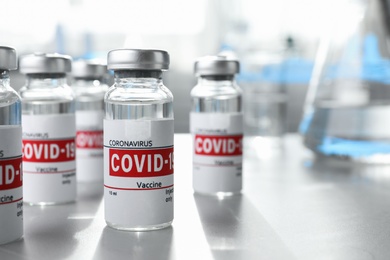 Glass vials with COVID-19 vaccine on light table. Space for text