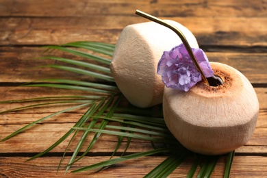 Fresh coconut with drinking straw and flower on wooden table. Space for text