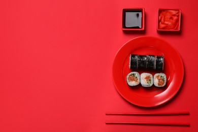 Tasty sushi rolls, soy sauce and ginger on red background, flat lay. Space for text