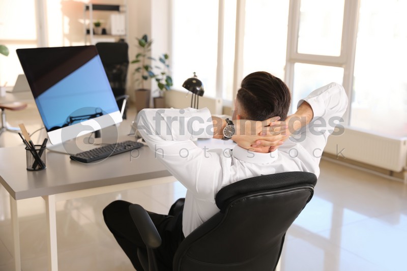 Photo of Businessman relaxing in office chair at workplace, back view