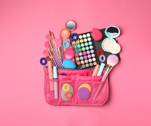 Cosmetic bag with makeup products and beauty accessories on pink background, flat lay