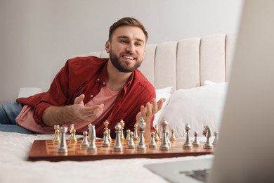 Young man playing chess with partner through online video chat on bed at home