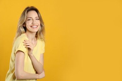Portrait of happy young woman with beautiful blonde hair and charming smile on yellow background. Space for text