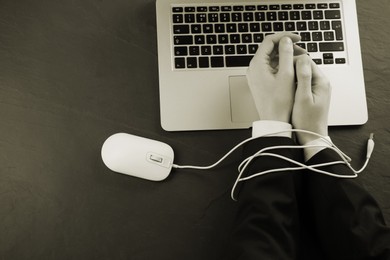 Image of Top view of woman with her hands tangled in cable of computer mouse at black table, sepia effect. Internet addiction