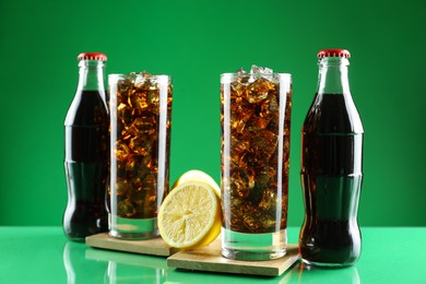 Bottles and glasses of refreshing soda water on green background