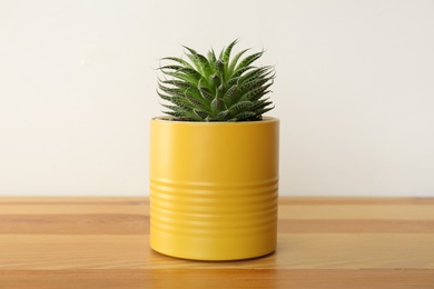 Houseplant in yellow tin can on wooden table, closeup