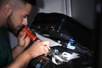 Repairman with flashlight fixing modern printer indoors
