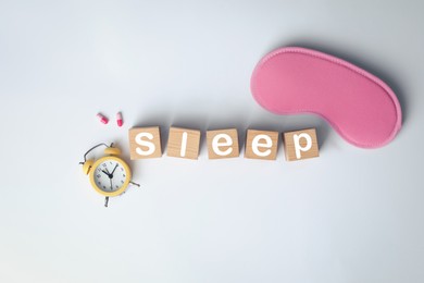 Word Sleep made of wooden cubes near blindfold, pills and alarm clock on white background, flat lay. Insomnia treatment